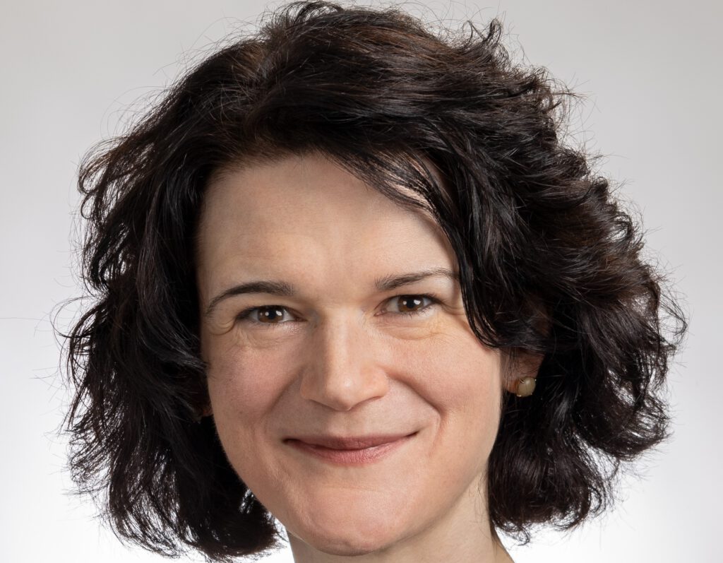 Frau mit lockigem, dunklem Haar und freundlichem Lächeln, in einem professionellen Kontext.