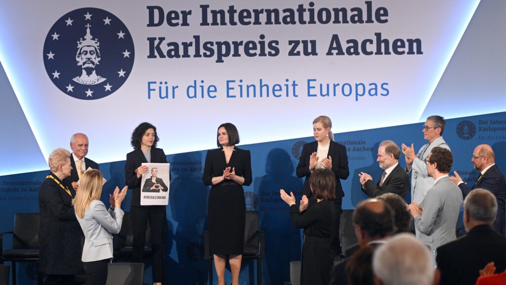 Verleihung des Internationalen Karlspreises zu Aachen, mehrere Personen applaudieren, eine Frau hält ein Plakat mit der Aufschrift "Friedenspreis".