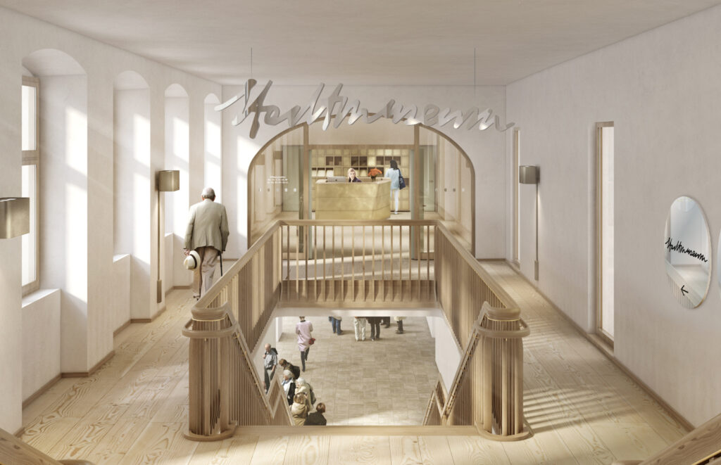 Heller Innenraum mit Holzgeländer und Treppe, Menschen im Hintergrund, moderne Beleuchtung und Schriftzug an der Decke